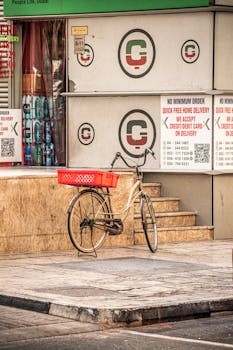 Vintage bike with a red basket parked on a city sidewalk corner near a shop sign in Dubai.