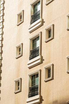 Close-up of a modern apartment building facade with windows and decorative railings in warm sunlight.