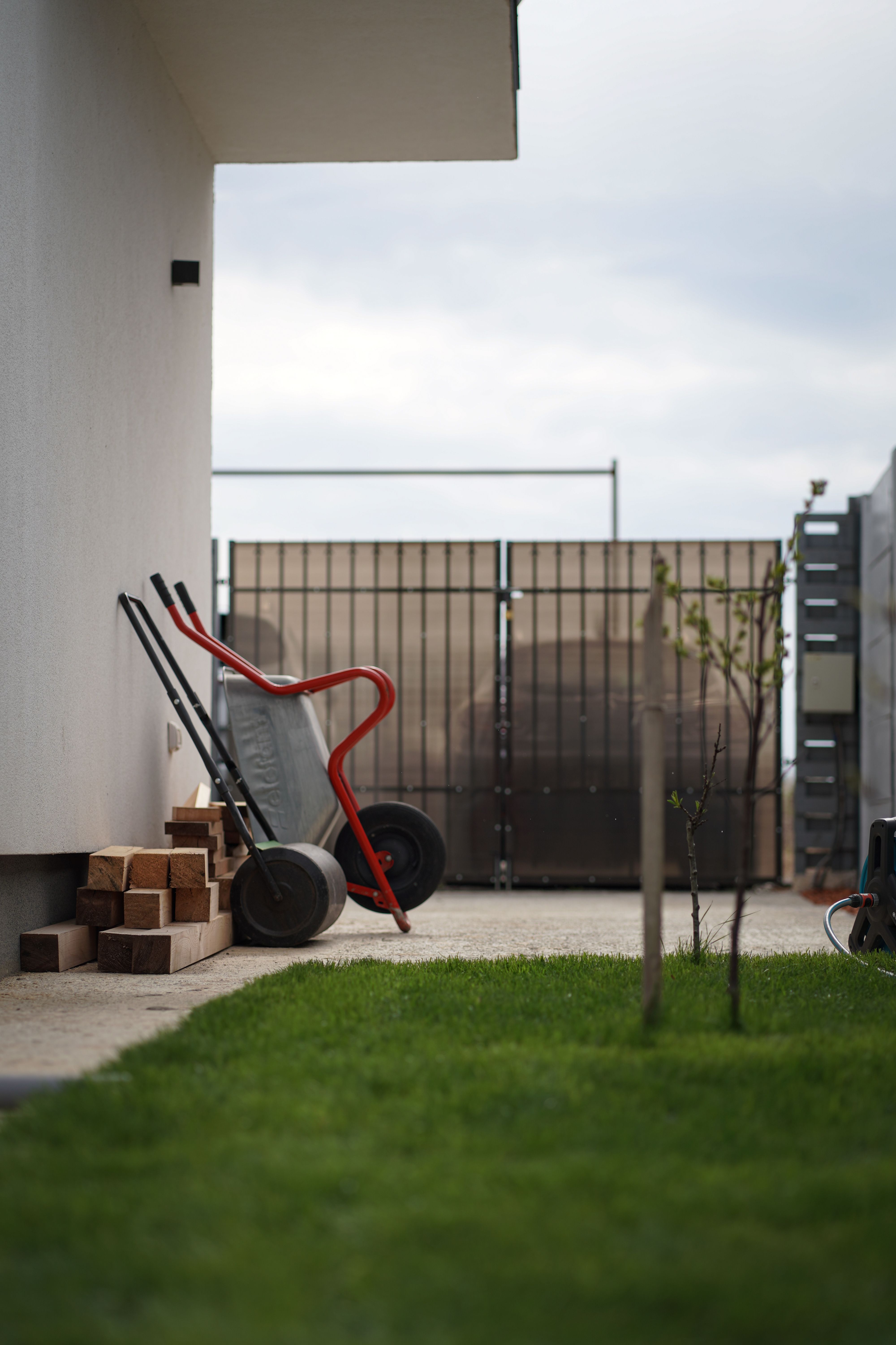 Side view of a yard with a wheelbarrow, stacked firewood and green grass beside a modern house.
