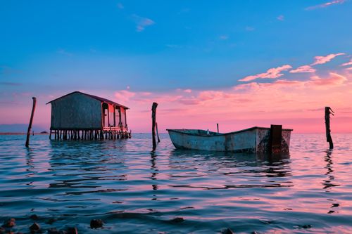 Free Tranquil scene of a rustic stilt house and boat on water during sunset in Yumurtalık, Türkiye. Stock Photo