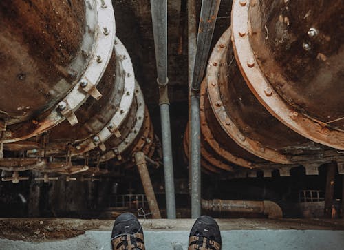 Pipes under Shoes of Person Standing at Factory