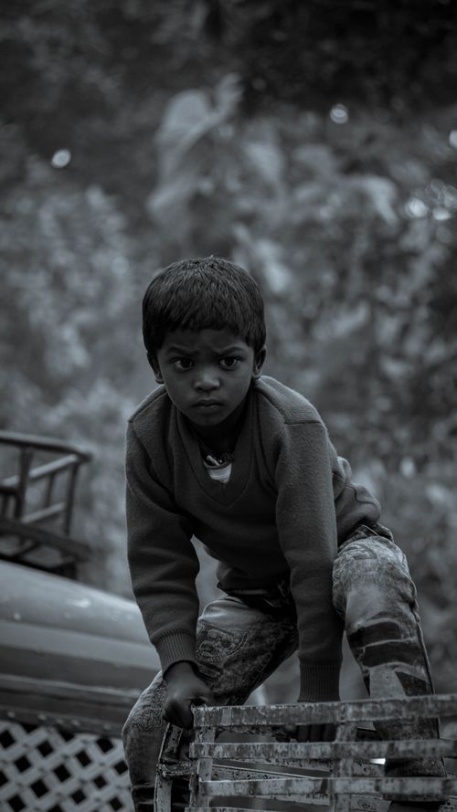 Free A young boy in India climbs on a metal crate in an outdoor setting with focus on his expression. Stock Photo