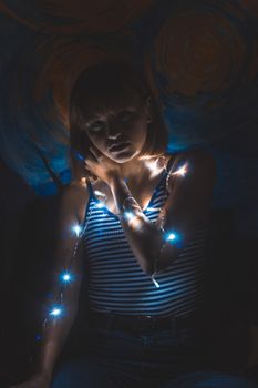 在黑暗背景下，串灯照亮了一位女性的艺术肖像，营造出喜怒无常的氛围