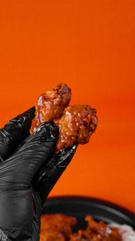 Close-up of glazed chicken wings held against a vibrant orange background.