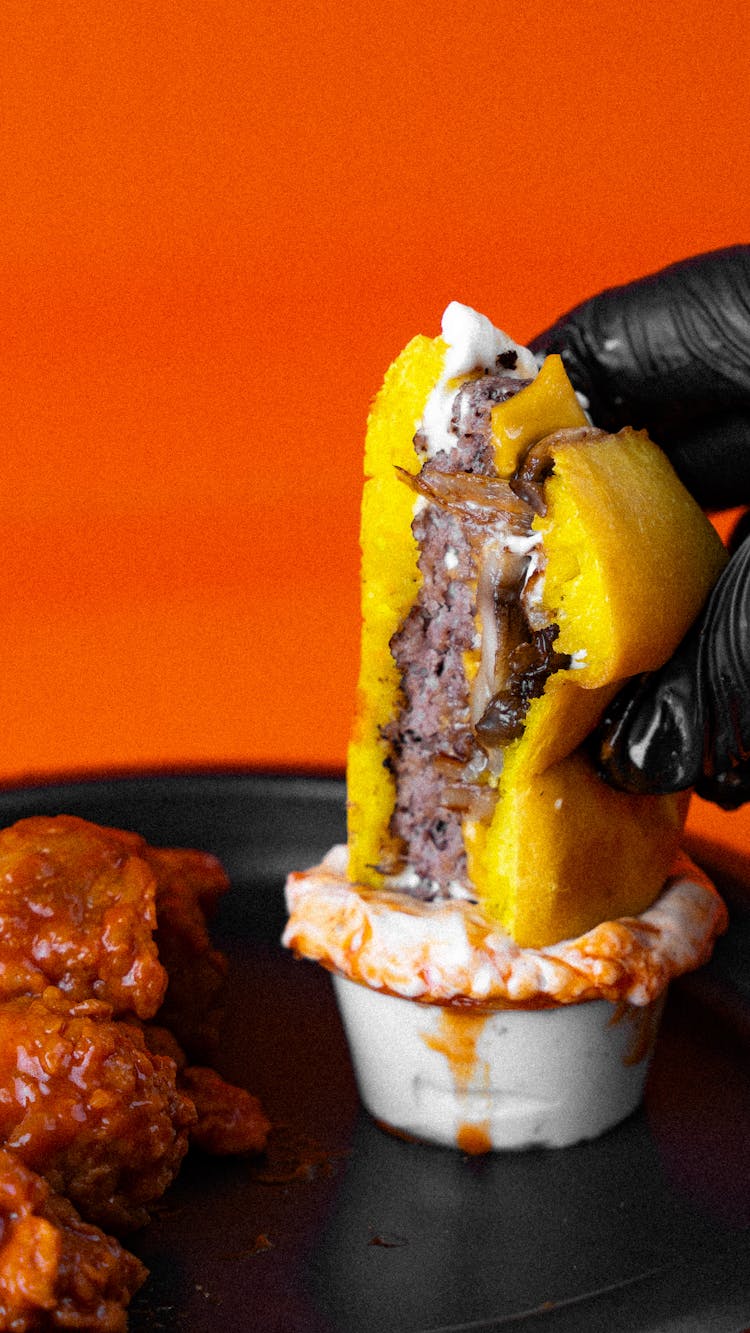 Hand In Black Gloves Dipping Cheeseburger In Mayo 