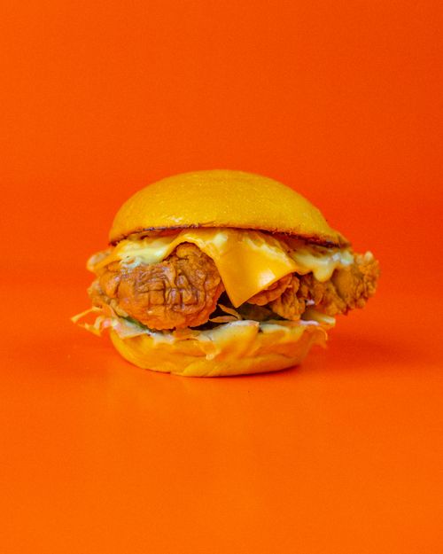 Free Delicious chicken burger with cheese on orange background, perfect for fast food themes. Stock Photo