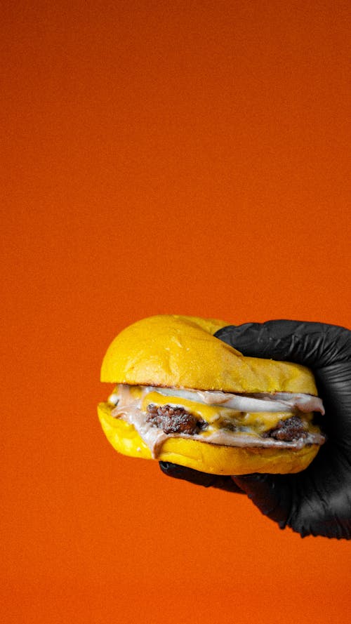 Hand in Black Gloves Holding Cheeseburger on Orange Back