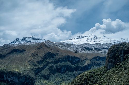 Free Breathtaking view of snow-covered mountains with lush green valleys below under a cloudy sky. Stock Photo