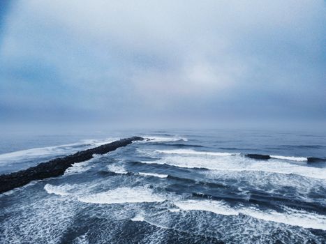 A captivating aerial shot of waves crashing on a rocky shore under an overcast sky.