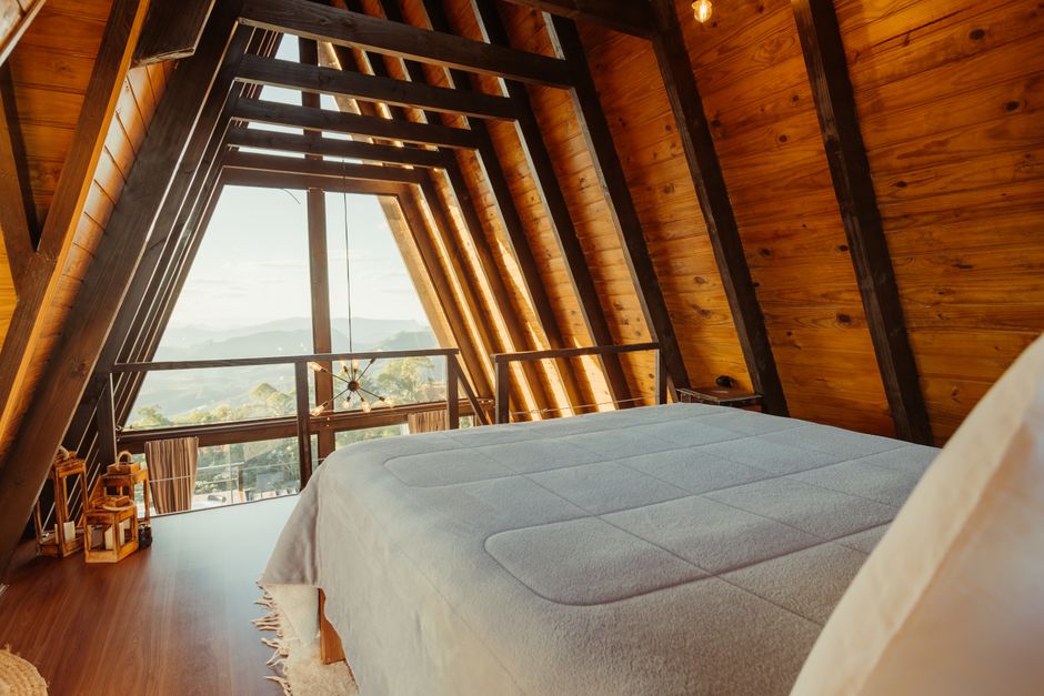 A serene A-frame bedroom interior with wooden walls and a scenic view from the window, located in Santa Teresa, Brazil.