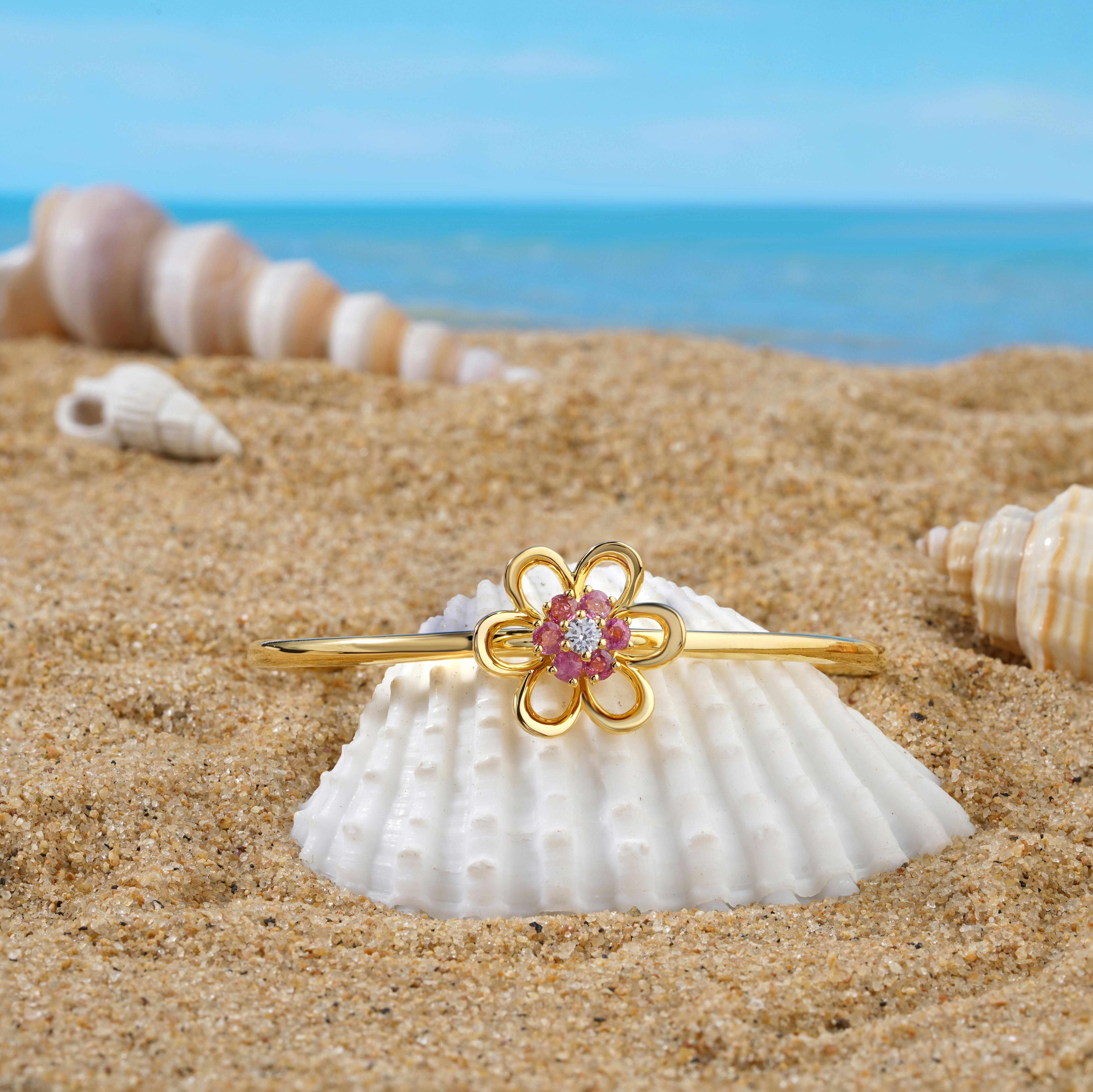 Elegant gold bracelet with floral design displayed on seashells at a sunny beach.