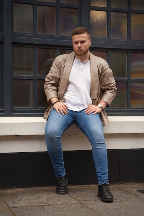 Man in Jacket Sitting on Wall near Windows