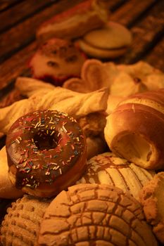 A warm-toned close-up of diverse Mexican pastries including a chocolate donut with sprinkles.