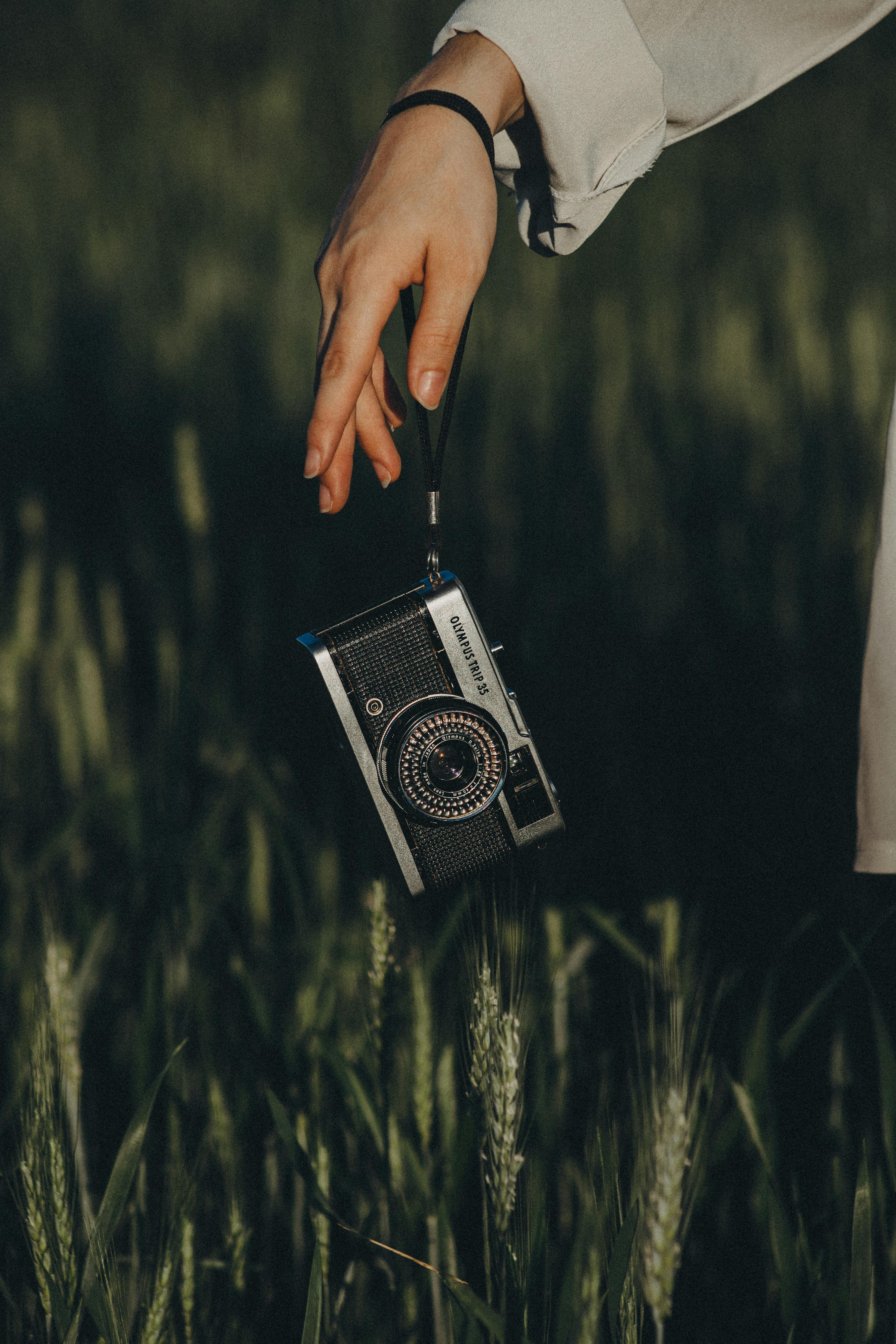 Close-up of a vintage camera held by a hand amidst green grass outdoors in Brazil.