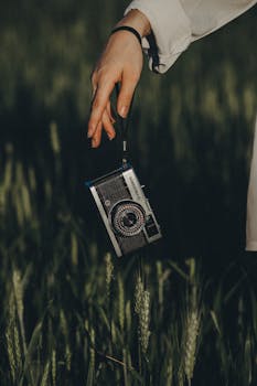 Close-up of a vintage camera held by a hand amidst green grass outdoors in Brazil.