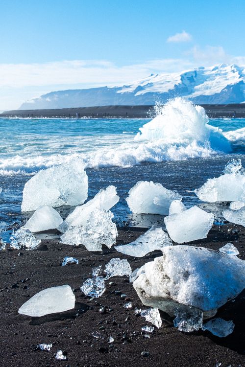 Free Captivating winter scene of icebergs on a black sand beach with ocean waves crashing. Stock Photo
