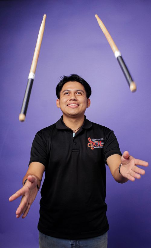 Free A smiling man skillfully juggling drumsticks in front of a vibrant purple background. Stock Photo