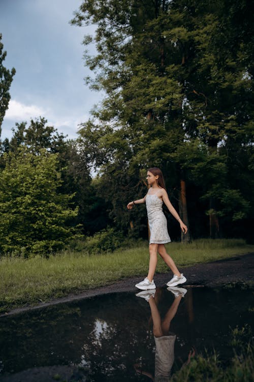 Teenager Girl in Summer Dress and Trainers Walking on a Rural Road with Rain Puddle