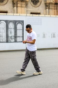 Young man in urban fashion walking on city streets, wearing cargo pants and sunglasses.