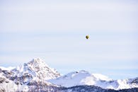 蔚蓝的天空下，一个孤独的热气球漂浮在白雪皑皑的山峰之上