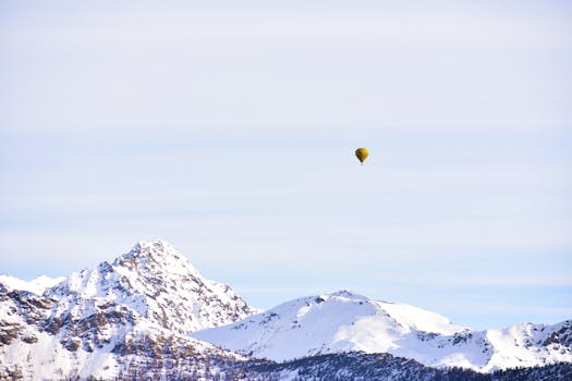 蔚蓝的天空下，一个孤独的热气球漂浮在白雪皑皑的山峰之上