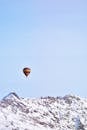 一只色彩缤纷的热气球飘过白雪皑皑的雄伟山脉，背景是蔚蓝的天空