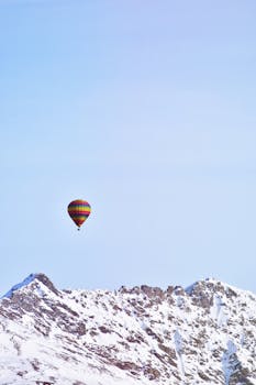 一只色彩缤纷的热气球飘过白雪皑皑的雄伟山脉，背景是蔚蓝的天空