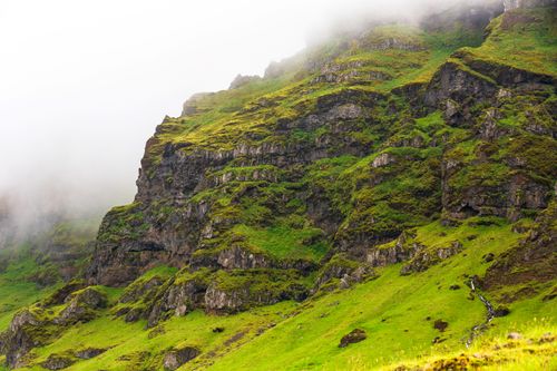Free Serene view of an eroded, mist-covered mountain side with lush green grass. Stock Photo
