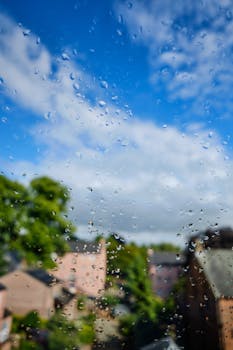 Close-up of raindrops on a window, with a blurred view of buildings and trees in Penrith, England.