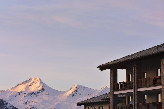 Snow-capped mountains at sunset, viewed from rustic chalets, capturing winter's beauty.