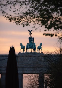 Silhouette of Brandenburg Gate at sunset in Berlin, Germany, framed by trees.