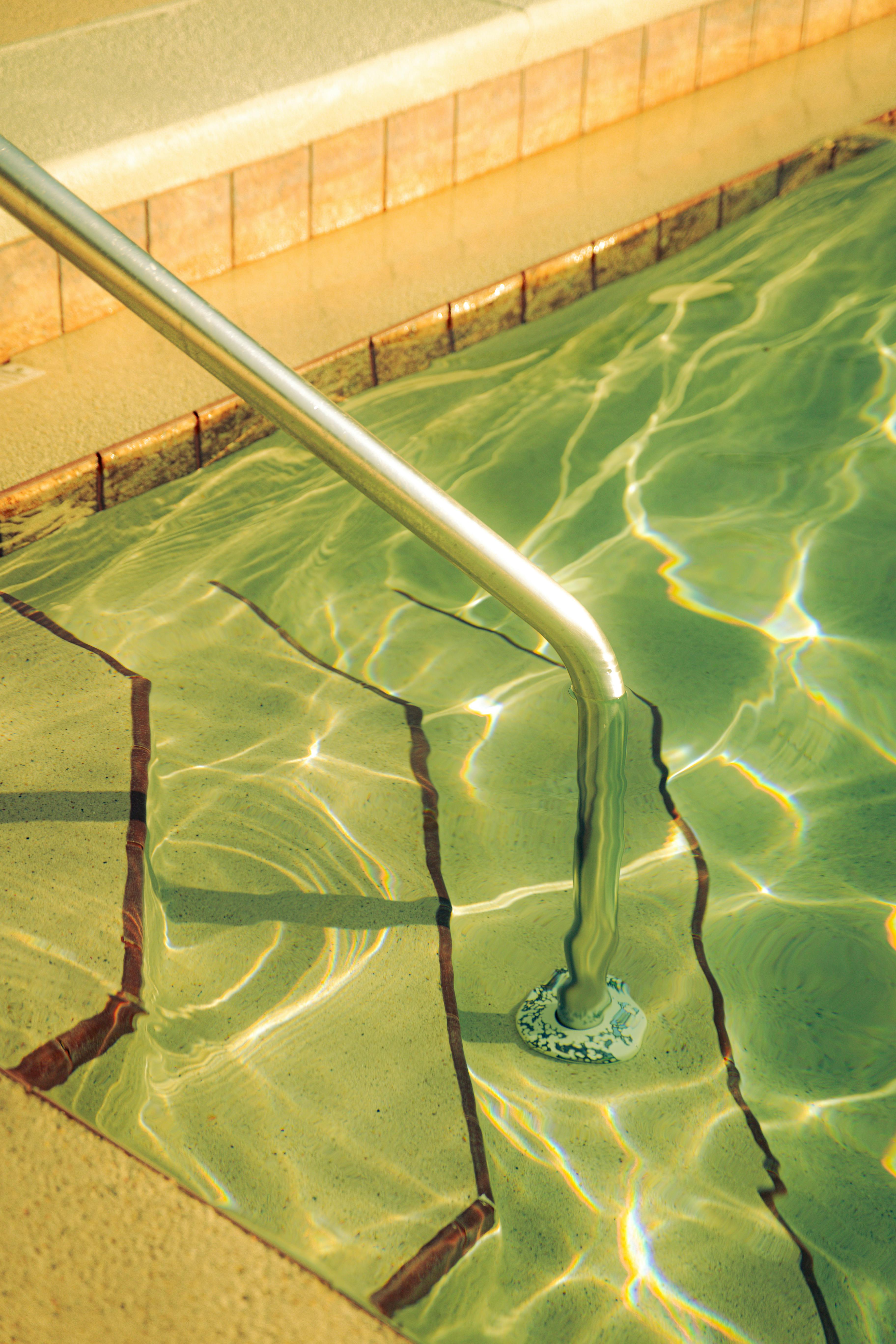 Sunlit swimming pool steps with water reflections and railings.