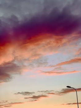 Dramatic purple and orange clouds at sunset over a streetlight, showcasing nature's beauty.