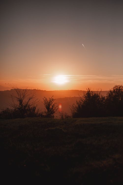 Free A stunning sunset over hills with a silhouette of trees, capturing the tranquil beauty of nature at dusk. Stock Photo