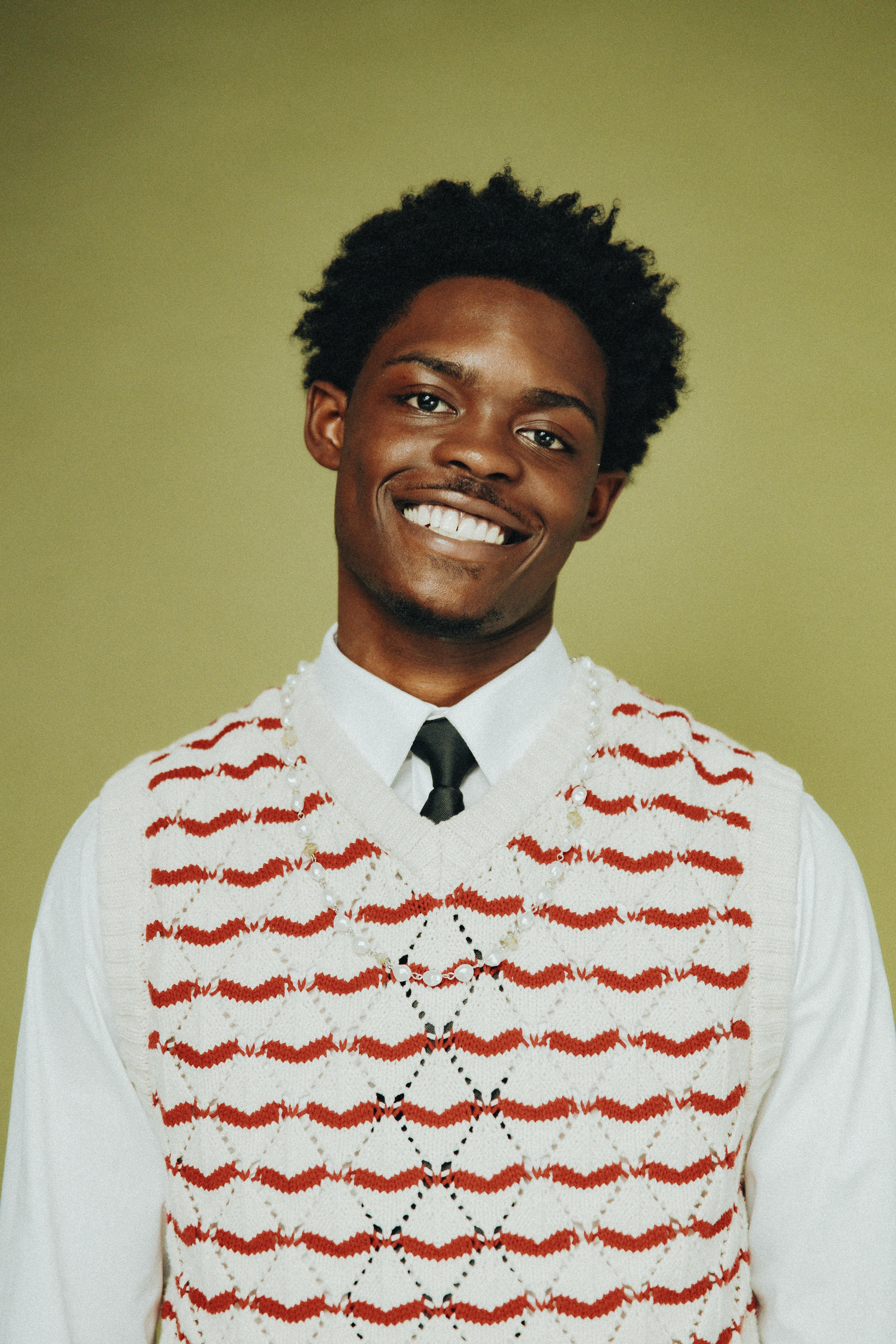 A cheerful young man smiling in a studio portrait with a colorful sweater.