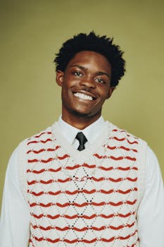 A cheerful young man smiling in a studio portrait with a colorful sweater.