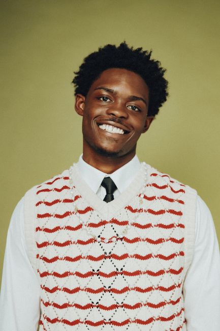 A cheerful young man smiling in a studio portrait with a colorful sweater.