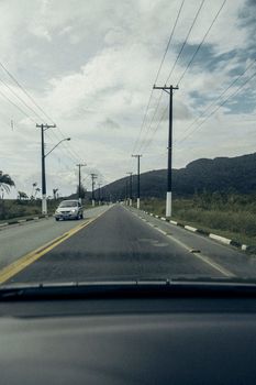 View from a car's windshield of a rural road with power lines, mountains, and clouds.