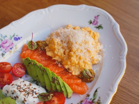 Delicious gourmet breakfast with scrambled eggs, smoked salmon, and fresh avocado on a floral plate.