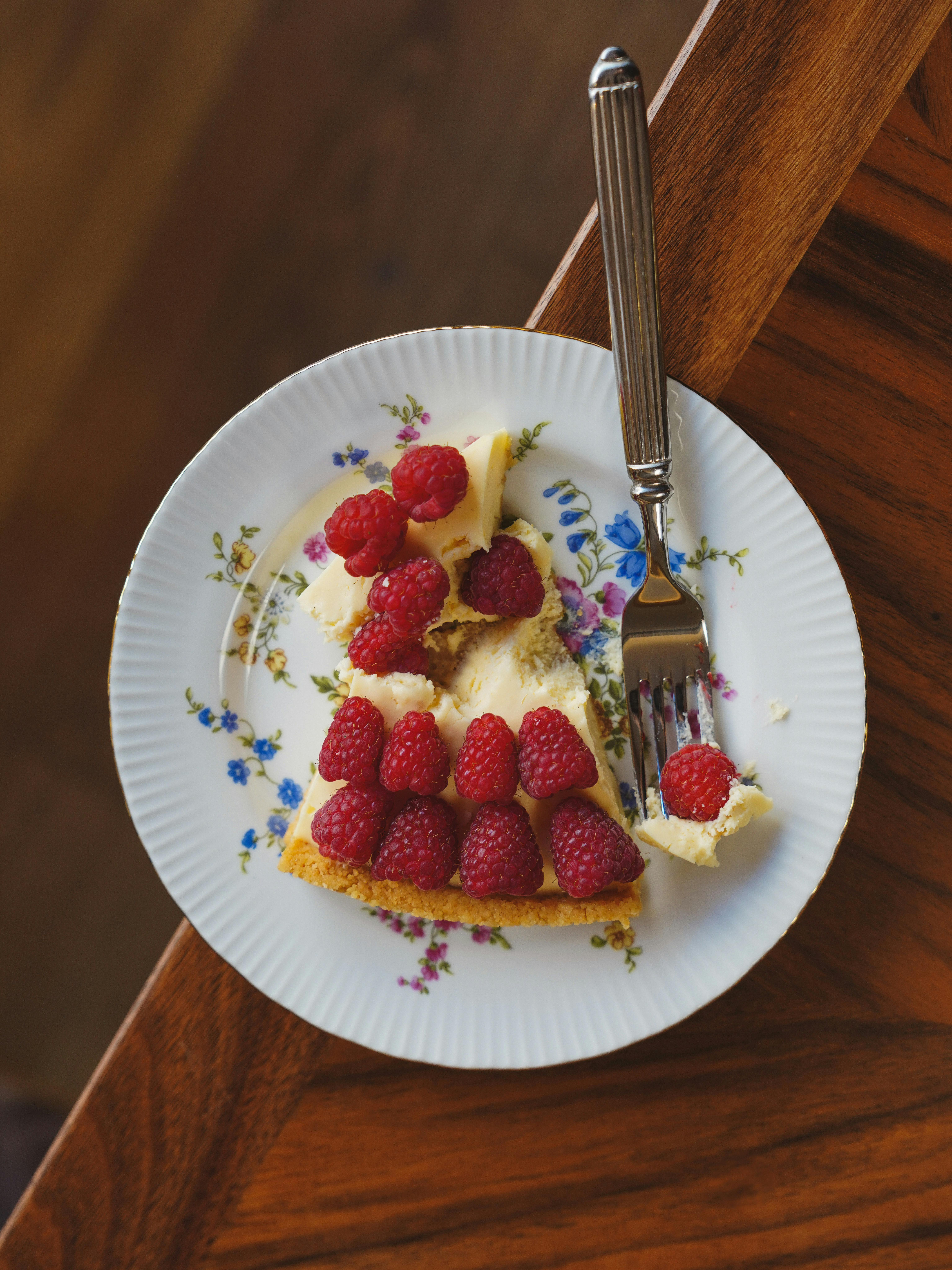 Slice of homemade cake with raspberries on a floral plate, perfect for food photography.