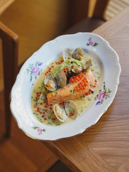 Delicious salmon filet with caviar, clams, and creamy sauce served on a floral plate.