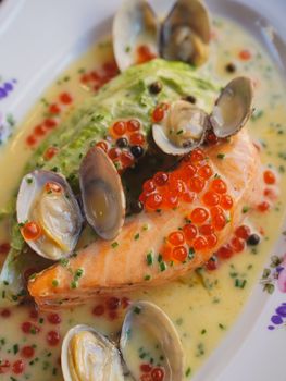 Delicious salmon fillet with clams, caviar, and vegetables in a creamy sauce.