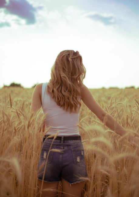 Back view of a woman enjoying a carefree walk through sunlit wheat fields, capturing summer freedom.