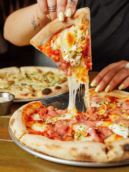 A mouthwatering slice of ham and cheese pizza being lifted with visible cheese pull.