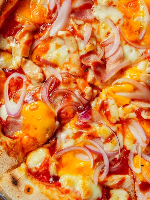 Free A mouth-watering close-up of a cheesy pizza slice garnished with onions and ham. Stock Photo