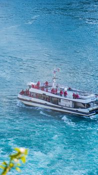 A tour boat with passengers in red raincoats cruises the turquoise waters near Niagara Falls.