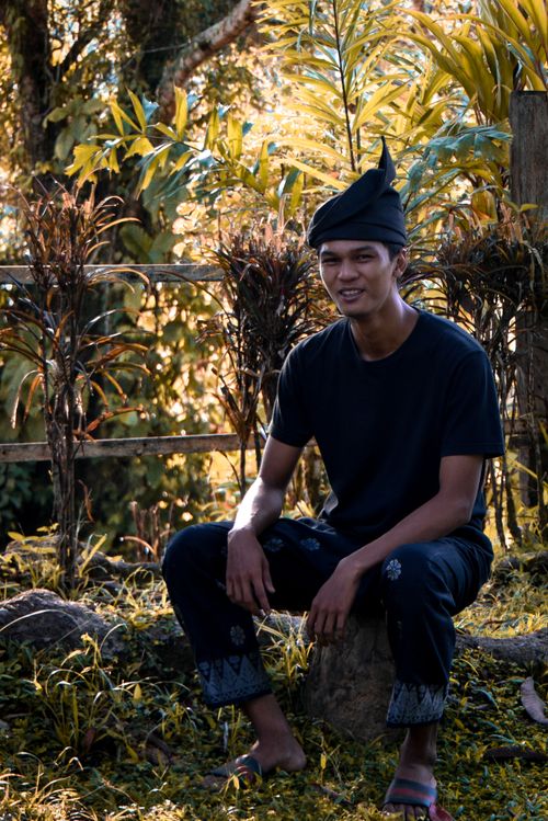 Free A young man in traditional attire smiling outdoors amidst lush tropical vegetation. Stock Photo