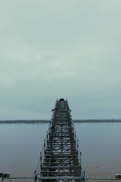 Free A metal bridge stretches over a river under a cloudy sky in Rosario, Santa Fe, Argentina. Stock Photo