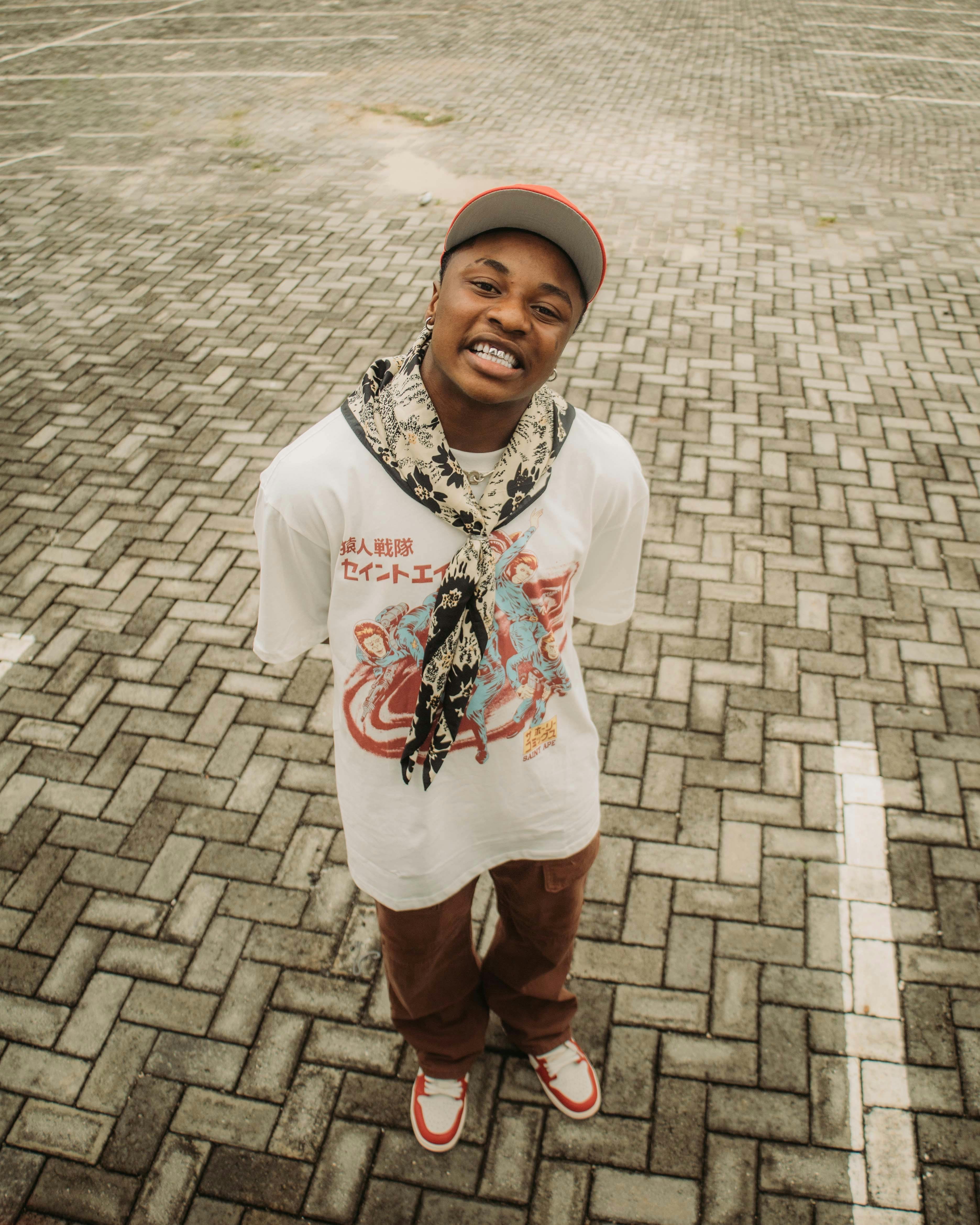 Young man in stylish streetwear posing outdoors on a paved surface.