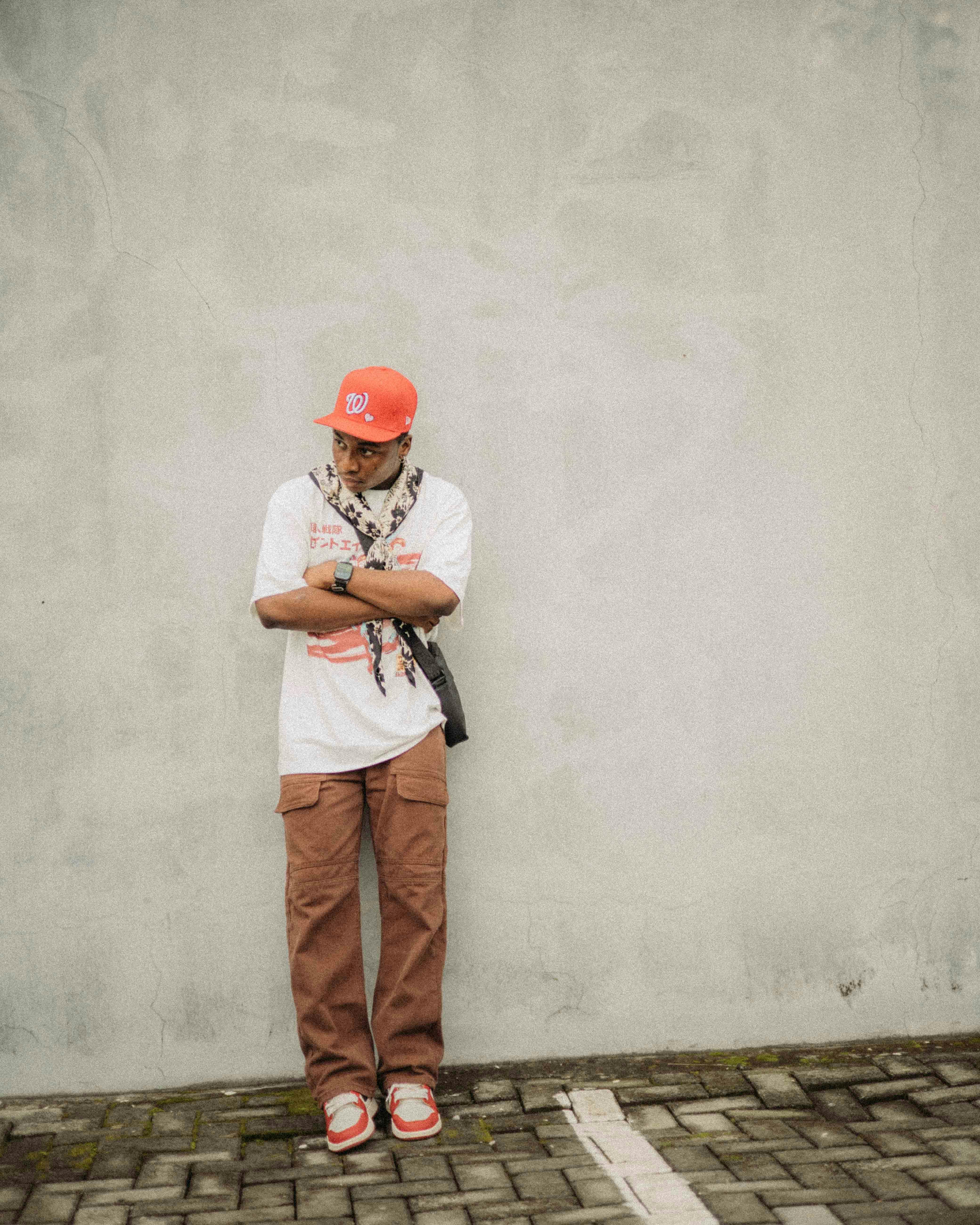 Young man in fashionable casual wear with orange highlights against a textured urban wall.